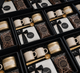 Corporate coffee gift box featuring artisan coffee, two ceramic mugs, a gold coffee scoop, scented candle, and chocolate-covered pretzels, thoughtfully curated for client and corporate gifting.