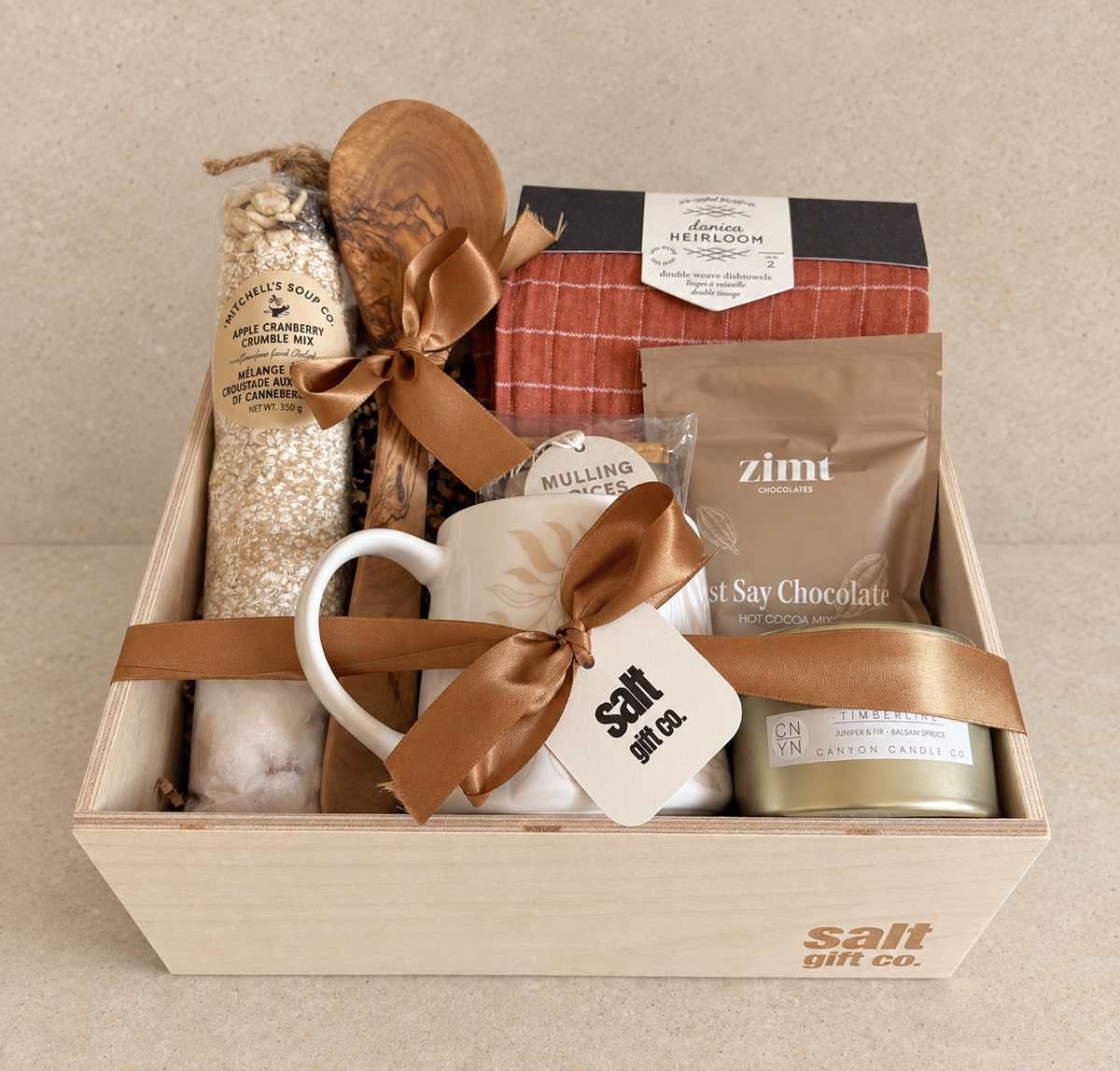 Handmade SALT Gift Co. holiday gift box with apple cranberry crumble mix, mulling spices, Zimt hot cocoa, a Canyon Candle Co. candle, a Danica Heirloom dishtowel, olive wood servers and a mug