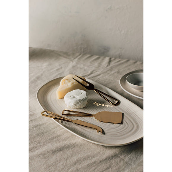 A Warm Welcome housewarming gift basket featuring a woven throw blanket, wooden serving board and cheese knives, olive oil, scented soap, candle, and gourmet chocolates, arranged in a natural woven basket.