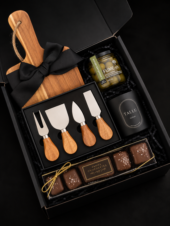Luxury corporate gift box featuring an acacia serving board, wooden-handle cheese knife set, gourmet olives, and artisan chocolates, arranged in a black gift box with black ribbon.
