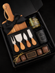 Luxury corporate gift box featuring an acacia serving board, wooden-handle cheese knife set, gourmet olives, and artisan chocolates, arranged in a black gift box with black ribbon.