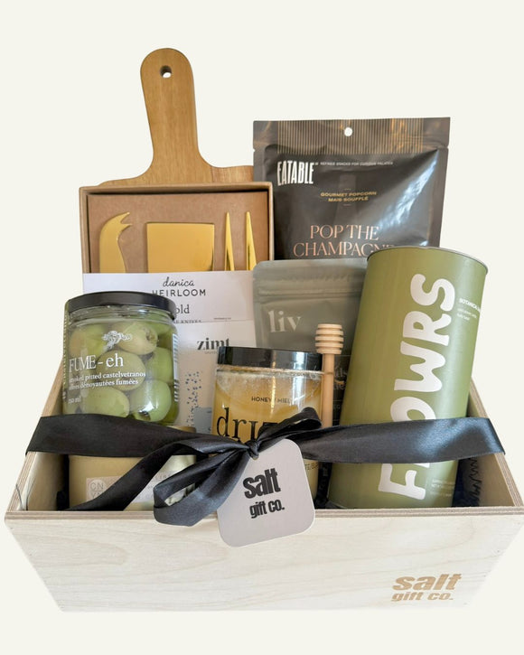 local vancouver canadian Gift basket with various items including a cutting board, charcuterie cheese knives, candles, tea, olives, honey, nuts.
