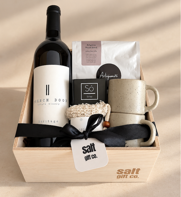 A curated gift basket in a light wood box from Salt Gift Co., featuring a bottle of French Door Winery red wine, Artigiano coffee, an SÓ Soap bar, espresso mug.